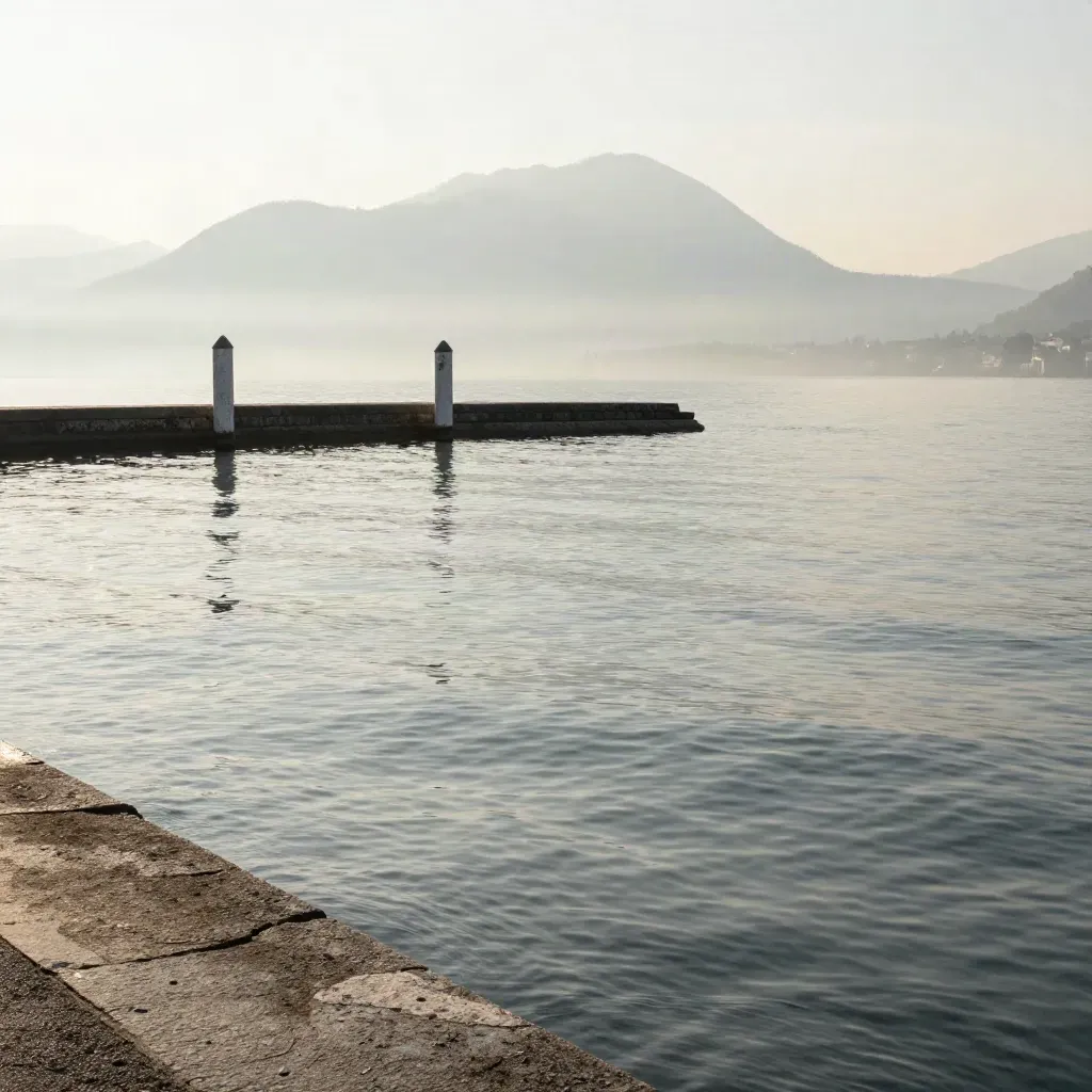 Il Lago di Como al mattino con acqua calma e profili di Varese in lontananza.